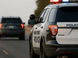 Hanford Police patrol SUV in pursuit of a dark colored vehicle on a rural two lane highway with emergency lights activated surrounded by dry grass and roadside trees capturing the intensity of